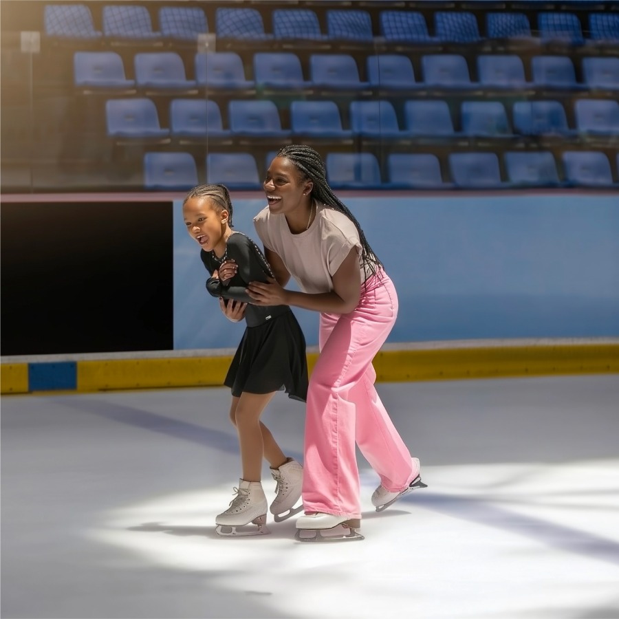 Mother helping her daughter ice skate at an indoor rink.