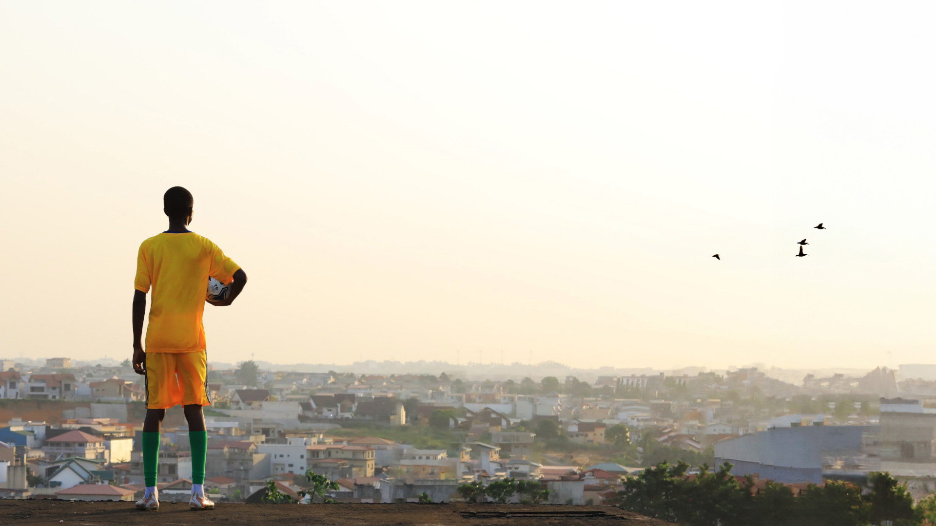 A football player holds the ball and looks at the morning city from the roof